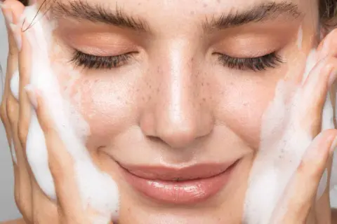 Visage de femme aux yeux fermés, profitant d'un nettoyage en profondeur avec de la mousse sur les joues.