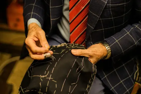 Sarto esperto cuce a mano, mostrando diversi tipi di polsini camicia. Dettagli sartoriali e precisione.