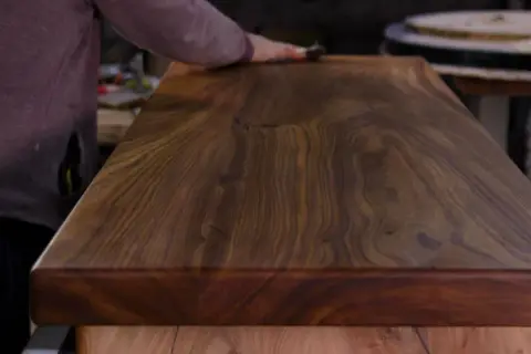 Main d'artisan polissant un plateau en bois exotique pour un entretien intérieur parfait.
