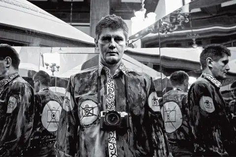 Krzysztof Miller w lustrzanym odbiciu, z aparatem na szyi, w koszuli z motywem oka.