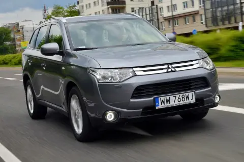 Szary Mitsubishi Outlander 3 jedzie po miejskiej drodze.