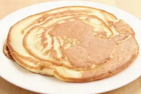 Ein goldbrauner Pfannkuchen ohne Ei auf einem weißen Teller, perfekt für ein leichtes Frühstück.