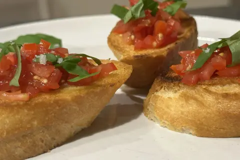 Drei Bruschetta-Scheiben mit Tomaten und Basilikum auf einem Teller.