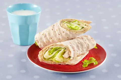 Två saftiga tonfisk wraps med krispig sallad på en röd tallrik, bredvid ett glas mjölk.