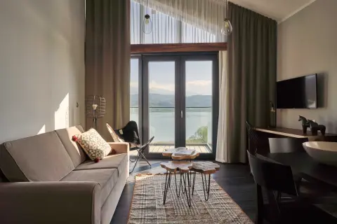 Przytulny pokój z widokiem na jezioro w hotelu Lake Hill Resort & Spa w Karkonoszach. Sofa, stoliki kawowe i krzesło motylkowe tworzą komfortową przestrzeń.