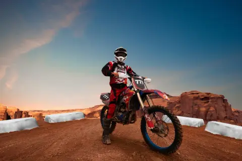 Motocyklista enduro w stroju i kasku na tle pustynnego krajobrazu z klifami i niebem.