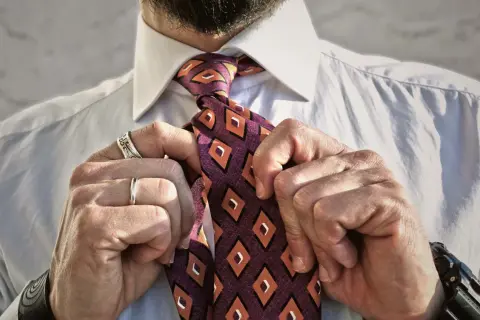 Uomo che sistema il nodo cravatta Eldredge, con camicia bianca e cravatta a rombi arancioni e viola.