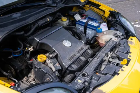 Silnik żółtego Alfa Romeo MiTo. Widoczny akumulator, obudowa filtra powietrza z logo marki i płyny eksploatacyjne.