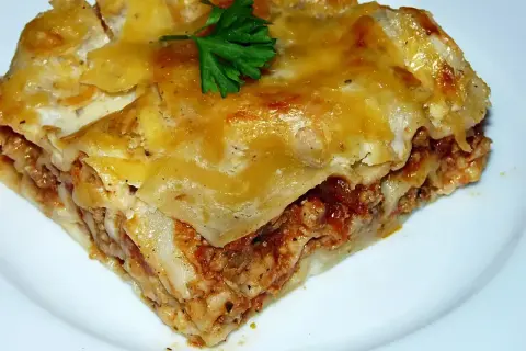 Pyszny kawałek lasagne z mięsem mielonym, zrumieniony ser i świeża natka pietruszki. Idealny przepis na obiad.