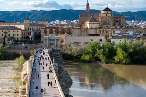 El Puente Romano de Córdoba, con la Mezquita-Catedral al fondo, es lo mejor de Córdoba. Gente pasea por el puente sobre el río Guadalquivir.