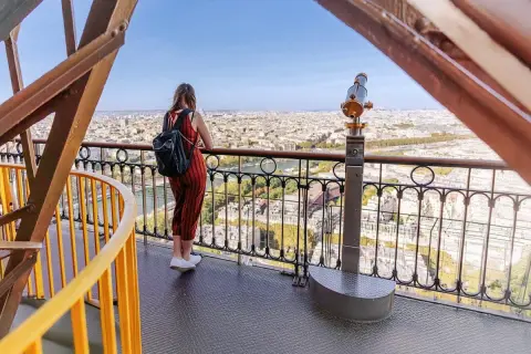 En kvinna med ryggsäck njuter av utsikten över Paris från Eiffeltornet. Hon undrar nog hur många trappsteg har Eiffeltornet.
