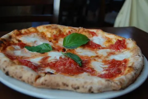 Pizza margarita recién horneada, con tomate y mozzarella fundida, decorada con hojas de albahaca fresca. ¡Una delicia que te hará buscar las mejores pizzerías Zaragoza!
