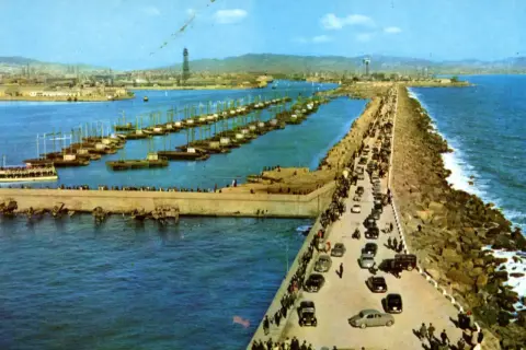 El rompeolas de Burela, con barcos alineados y coches circulando, protege la costa de las olas.