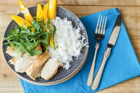Idealne danie, co jeść po treningu: grillowany kurczak, ryż, mango i rukola na talerzu.