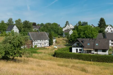 Fachwerkhäuser säumen den malerischen fachwerkweg Ruppichteroth, eingebettet in grüne Hügel unter blauem Himmel.