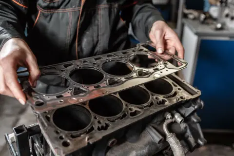 Mechanik przygotowuje wymianę uszczelki pod głowicą silnika. Nowa uszczelka czeka na montaż.
