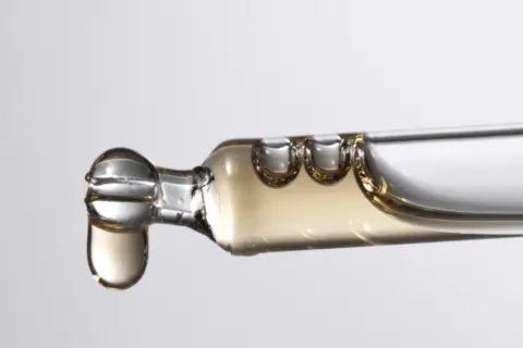 Tropfen eines goldenen Serums, das Bisabolol enthält, fallen aus einer Pipette.