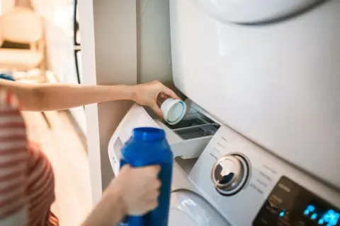 Dłoń wlewa płyn do prania do szufladki pralki. Właściwe miejsce, gdzie wlać płyn do prania, jest kluczowe dla czystych ubrań.