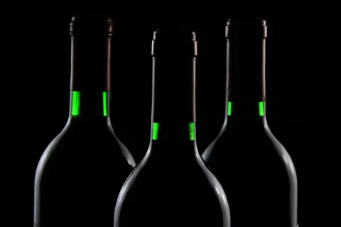 Trzy butelki z zielonymi akcentami, sugerujące dobre wino wytrawne czerwone. Ciemne tło podkreśla elegancję.