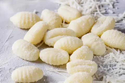 Frische Gnocchi, bereit für köstliche Gnocchi Rezepte, liegen auf einem grauen Untergrund, bestreut mit etwas geriebenem Käse.