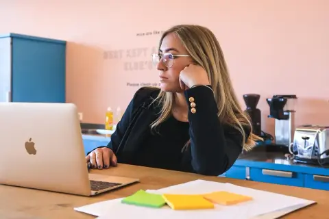 Kobieta w okularach zastanawia się, jak zatrudnić stażystę, siedząc przy laptopie.