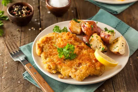Goldbraunes Schnitzel, perfekt paniert, mit Rosmarinkartoffeln und Zitrone. So paniert man Schnitzel für ein köstliches Essen.