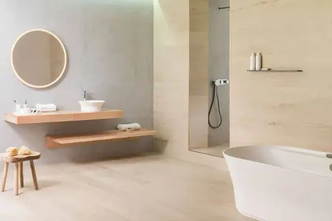 Baño moderno con lavabo flotante, bañera blanca y ducha. El suelo de madera clara contrasta con los azulejos de la pared.