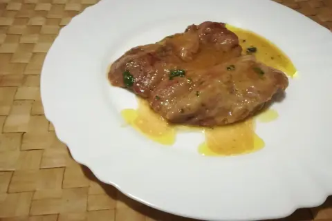 Due fettine di tacchino appetitose, immerse in una salsa dorata e profumata, servite su un piatto bianco.