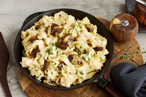 Cremiges Pasta Alfredo mit Pilzen, garniert mit Petersilie, serviert in einer Gusseisenpfanne.
