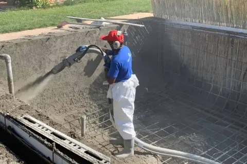 Un ouvrier projette du béton pour créer un bassin en béton étanche. La structure métallique est visible.