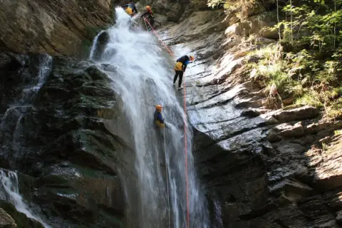 Descente en rappel le long de la cascade de Nyon. Des canyoneurs descendent une chute d'eau spectaculaire, entourés par la roche et la végétation luxuriante.