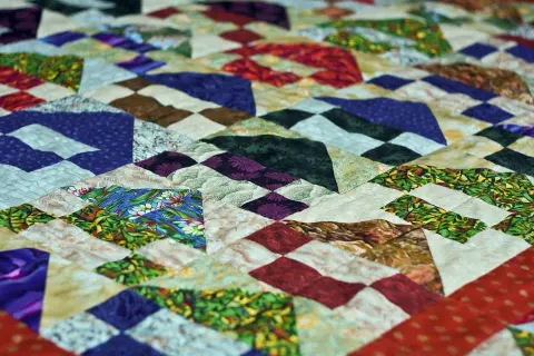 Kolorowy patchwork z geometrycznymi wzorami, wykonany techniką pikowania tkanin. Wzory przypominają góry i doliny.