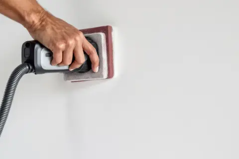 Main tenant utilise un aspirateur pour nettoyer le mur après ponçage.