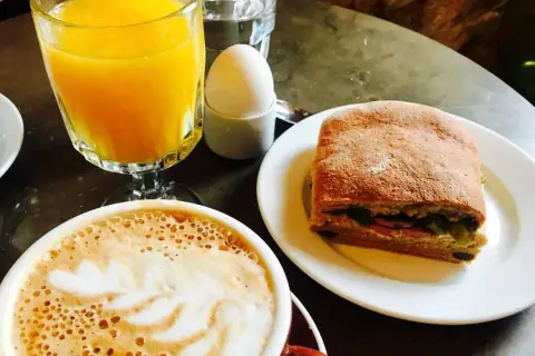 En kopp kaffe med lattekonst, apelsinjuice, ett kokt ägg och en macka. En perfekt frukost som ger en känsla av comfort food.