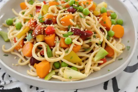 Assiette de nouilles sautées colorées avec carottes, petits pois, poivrons et garniture de sésame. Une recette facile et savoureuse.