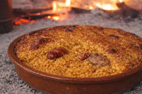 Arroz con costra recién hecho, con trozos de carne y salchicha, cocinándose a la leña.