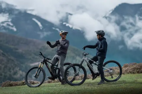 Dos ciclistas con cascos y bicicletas ebike en un paisaje montañoso, listos para explorar nuevas rutas.