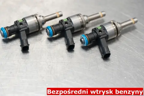 Trzy wtryskiwacze do silnika benzynowego z bezpośrednim wtryskiem (GDI) leżą na metalowej powierzchni.