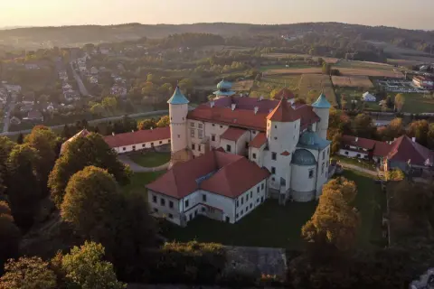 Zamek w Wiśniczu, otoczony zielenią i wzgórzami, prezentuje się majestatycznie o zachodzie słońca.