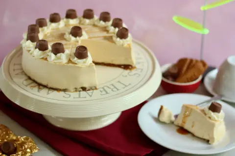 Eine köstliche Maxi King Torte, verziert mit Sahnetuffs und Schokostückchen, steht auf einem Tortenständer. Ein Stück ist bereits auf einem Teller angerichtet.