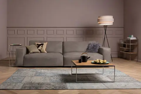Gemütliches Wohnzimmer mit einem Sofa in Farbe Taupe, einem Couchtisch mit Teekanne und Früchten, sowie einem Teppich.