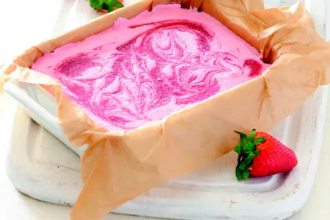 Różowe lody z mascarpone z wirami truskawkowymi w prostokątnym naczyniu wyłożonym papierem.
