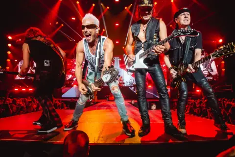 Zespół Scorpions na koncercie, grający swoje rockowe ballady. Wokalista z blond włosami i w okularach krzyczy do mikrofonu.