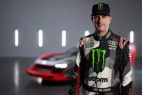 Ken Block, piloto de rally, posa con su traje de competición y un coche de Audi e-tron detrás.