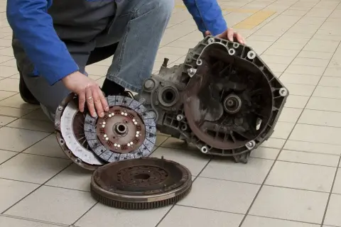Mechanik pokazuje rozłożony zestaw sprzęgła i skrzynię biegów. Uszkodzony wysprzęglik objawy mogą być różne, ale ten element jest kluczowy.