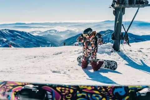 Dziecko w kolorowym kombinezonie przygotowuje się do zjazdu na snowboardzie. Idealne miejsce, gdzie na narty w Czechach z dziećmi.