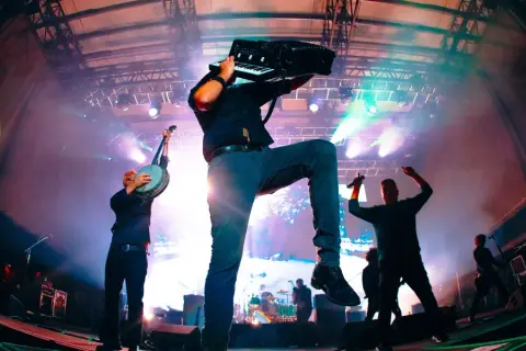 Energetyczny koncert Dropkick Murphys. Muzyk gra na akordeonie, inny na banjo, tłum szaleje.