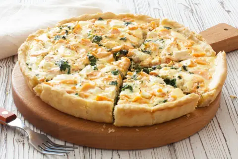 Pyszna tarta z łososiem, szpinakiem i serem feta, pokrojona na kawałki, na drewnianej desce.