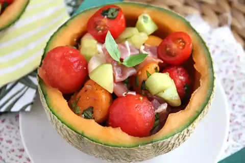 Erfrischender **Salat mit Melone**, Tomaten und Schinken, serviert in einer ausgehöhlten Honigmelone. Ein leichter Genuss!