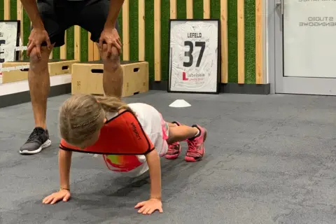 Dziecko wykonuje ćwiczenia na brzuch w domu, pod okiem trenera.